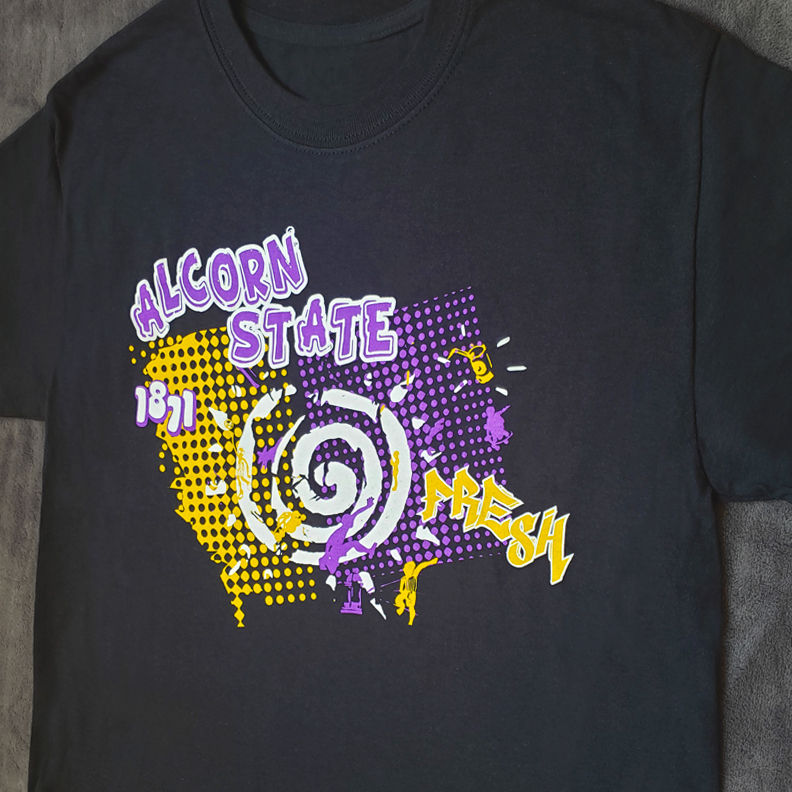 A black t-shirt with Alcorn State 1871 Fresh screen printed on the front. The graphic is speckled with yellow and purple dots, as well as a white sun and paint splatters.