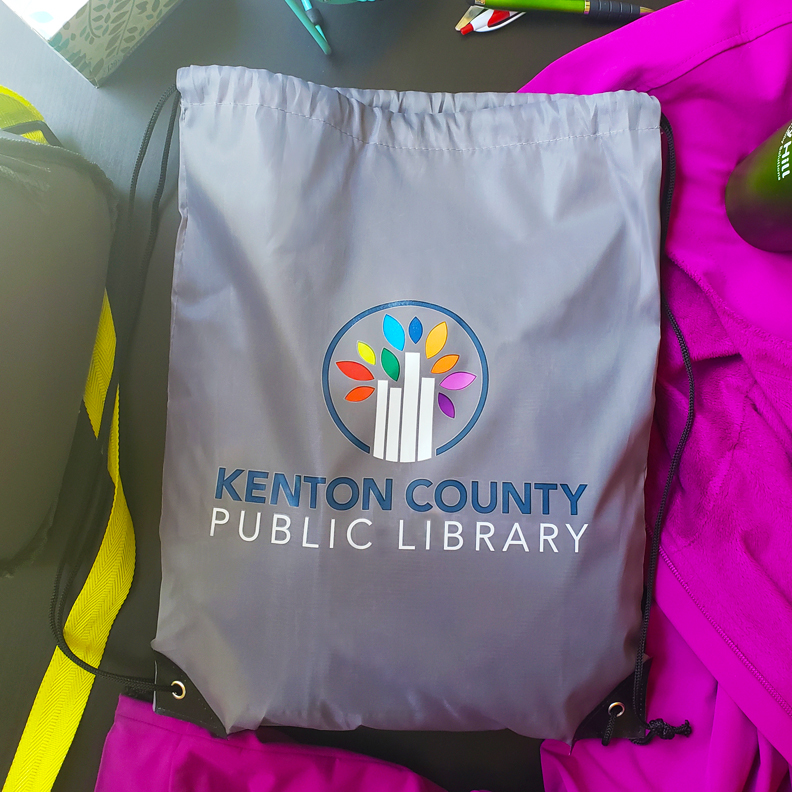 A gray drawstring bag with Kenton County Public Library's logo screen on the front.
