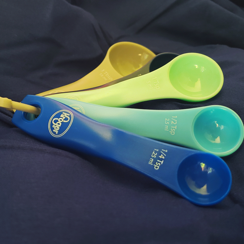 A set of multicolored measuring spoons with the Kroger logo on the handles.