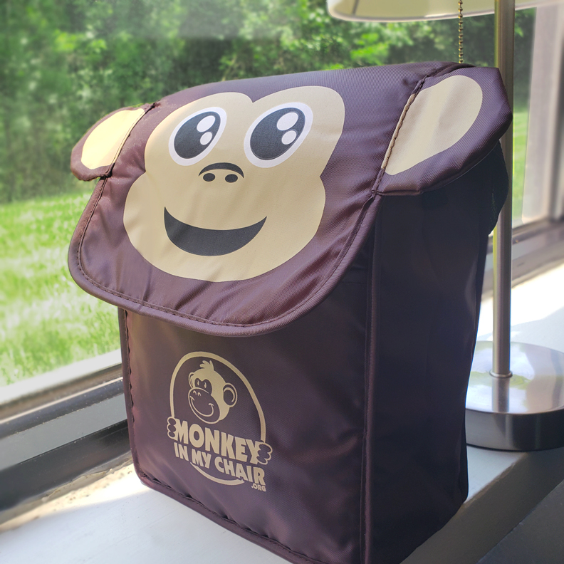 A lunchbox with a flap that has a cartoon monkey's face and ears. The logo 'Monkey in my Chair' is on the front.